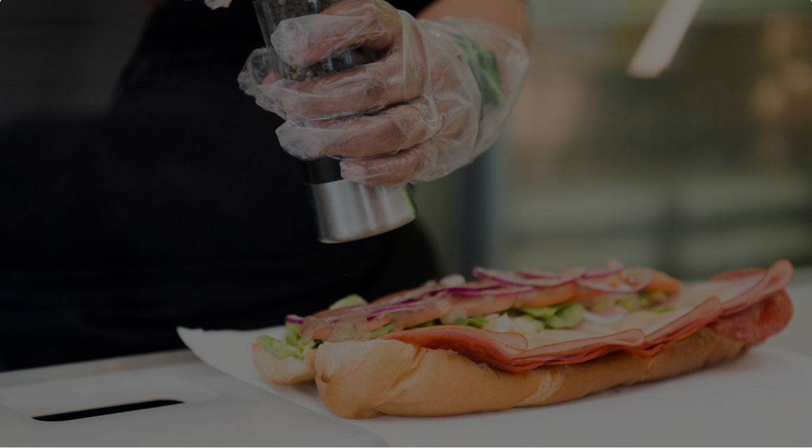 Sandwich artist seasoning a sandwich